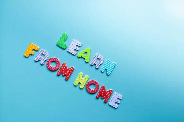 Words LEARN FROM HOME written of colorful wooden letters on blue background. Inscription learn from home on board with copy space. Homeschooling. Home education concept