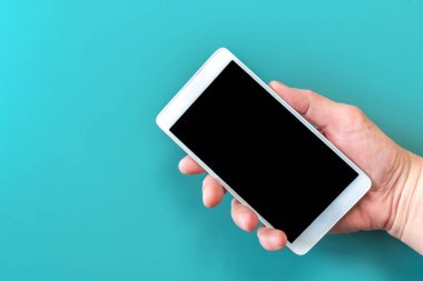 İzole edilmiş turkuaz arka planda el ele tutuşan telefonu kapat. Mavi arkaplanda boş siyah masaüstü ekranlı cep telefonunun el ele tutuşma görüntüsü. Mavi arkaplanda elinde akıllı telefon aygıtı.