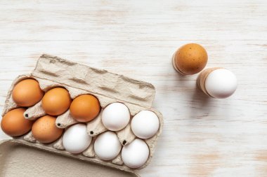 Kahverengi ve beyaz yumurtalarla dolu bir kutu ve ahşap masadaki tutacaklarda haşlanmış yumurtalar. Tahta arka planda geri dönüşümlü karton kutuda tavuk yumurtası. Karton kutuda serbest organik yumurta. Üst manzara, düz uzanma