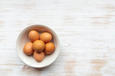Kasede organik yumurta var. Tahta masanın üzerinde kahverengi tavuk yumurtası tabağı. Tahta arka planda kasede yakın plan kahverengi yumurtalar. Üst manzara, düz yatış. Doğal sağlıklı gıda konsepti