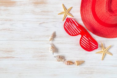 Seyahat ve tatil geçmişi kırmızı renkli şapka, gözlükler, deniz yıldızı ve deniz kabukları ile klasik ahşap bir tebessüm gibi. Gülümseyen insan yüzü olarak yaz aksesuarları. Düz konum, kopyalama alanı olan üst görünüm.