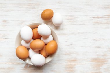 Kahverengi ve beyaz yumurtalar ahşap arka planda. Tabakta kahverengi ve beyaz tavuk yumurtaları var. Kasede organik yumurta var. Doğal sağlıklı gıda konsepti. Üst görünüm, düz görünüm, kopyalama alanı.