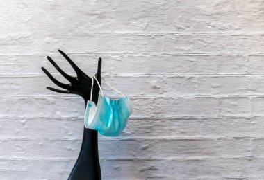 Siyah plastik el, beyaz duvar arkasında tek kullanımlık tıbbi yüz maskesi tutuyor. Mücevher için plastik manken elinde koruyucu yüz maskesi var. Koronavirüs salgınının modern güvenliği.