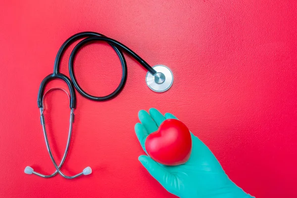 Tıbbi steteskop ve kırmızı arka planda kırmızı kalp taşıyan yeşil lastik eldiven. Eldiven ve stetoskop içinde kalbi izole bir şekilde yatıyordu. Organ bağışı konsepti için bir model. Boşluğu kopyala.