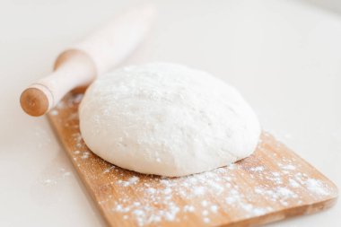 Ahşap bir kesme tahtasının üzerinde çiğ hamur. Yemek fotoğrafı tarifi fikri. Merdaneli pizza hamuru. Ev yapımı ekmek yapma süreci. Ev ekmeği pişirme.