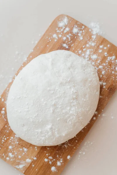 Ahşap bir kesme tahtasının üzerinde çiğ hamur. Yemek fotoğrafı tarifi fikri. Merdaneli pizza hamuru. Ev yapımı ekmek yapma süreci. Ev ekmeği pişirme.