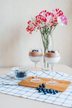 Lezzetli ve lezzetli İtalyan kremalı Panna Cotta sütlü ve çikolatalı chia tohumlarından yapılır. Taze yaban mersini ve çikolata kırıntılarıyla süslenmiş. Vazonun arka planında bir buket var. Sağlıklı beslenme. Süper yemek. 