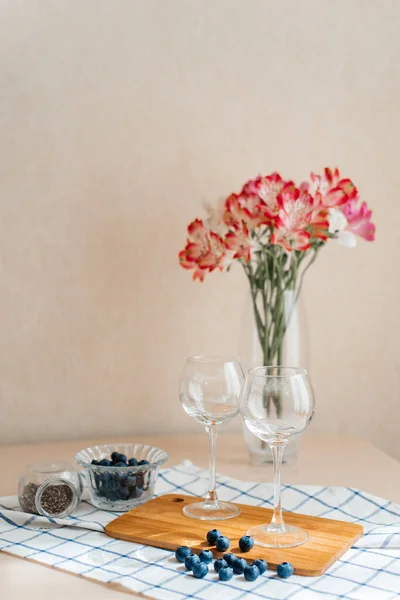 Kesme tahtasındaki iki bardak, bir vazo çiçekli taze yaban mersininin yanında yatıyor..