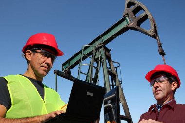 İki mühendisleri ile dizüstü bilgisayarlar petrol alanında / dizüstü bilgisayarlar açık havada pompa girişi yanındaki petrol sahasını kullanarak mühendisleri