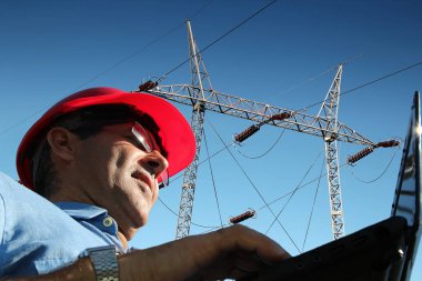 Mühendis ile dizüstü bilgisayar altında elektrik hatları / mühendis yüksek gerilim elektrik hatları yanında dizüstü bilgisayar kullanan kırmızı kask ile