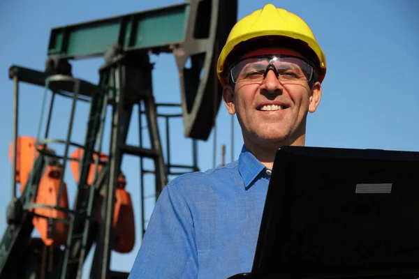 石油和石化工程 石油工程师与笔记本电脑在一个油田 监测工作的油泵千斤顶 石油工程师在户外使用便携式电脑 开发石油提取方法 — 图库照片