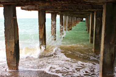 Bir balıkçı iskelesinin altında. Deniz gezinti güvertesinin desteği, köprünün altı, rıhtımın altı deniz suyu.