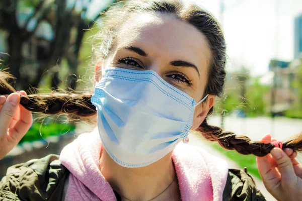 Koruyucu maske takmış neşeli bir kadının portresi saçlarını elinde tutuyor. Sokakta sosyal mesafeler.