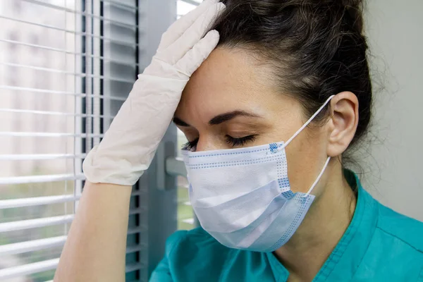 Yüzünde cerrahi maske ve doktor üniforması olan yorgun İtalyan doktor gözlerini kapadı ve başını yorgunluktan korudu..