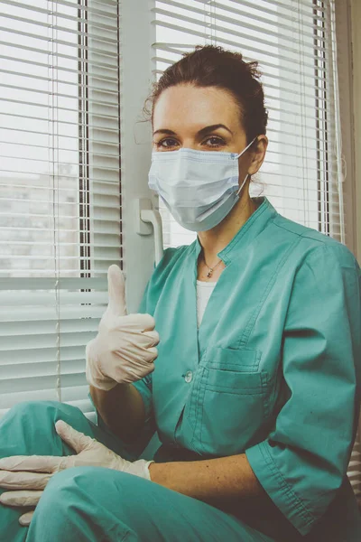 Cerrahi maskeli ve doktor üniformalı doktor parmak kaldırma hareketi gösteriyor.