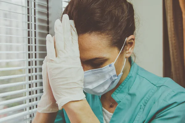 Portrait of Tired Doctor woman in medical mask, gloves and doctors suit closed her eyes