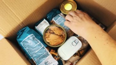 Bir adam Coronavirus salgını sırasında fakirlere bağış yapmak için yiyecek kutusu topluyor. Mısır gevreği, tereyağı, kavanozlardaki konserve yiyecekler. Market kartonlarının toplanması ve teslimatı.