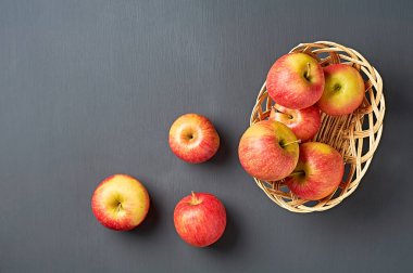 Dolu ahşap hasır sepetin yanında vitaminlerle dolu üç taze kırmızı olgun elma mutfaktaki eski, çizik beton masanın üzerinde yatıyor. Hasat ya da diyet konsepti. Mesaj için yer var. Üst görünüm