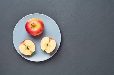 İki yarım, vitamin dolu bütün kırmızı olgun elmalar yuvarlak seramik tabakta ve mutfaktaki eski koyu çizik beton masada yatıyor. Hasat ya da diyet konsepti. Mesaj için yer var. Üst görünüm