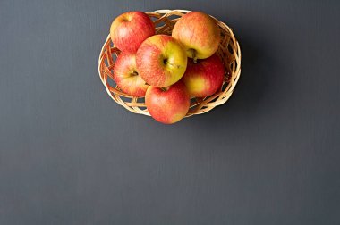 Vitamin dolu bir sürü taze kırmızı elma ahşap hasır sepetin içinde ve mutfaktaki eski koyu renkli beton masada yatıyor. Hasat ya da diyet konsepti. Üst görünüm