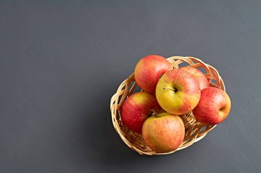 Vitamin dolu bir sürü taze kırmızı elma ahşap hasır sepetin içinde ve mutfaktaki eski koyu renkli beton masada yatıyor. Hasat ya da diyet konsepti. Metin için boşluk