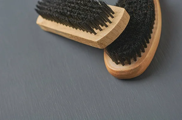 Two brushes with wooden handles for cleaning cloth, shoes, carpet or other textile product lies on dark scratched concrete desk. Space for text