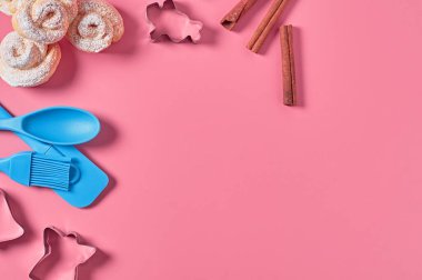 Metal şablonlar, plastik spatula, fırça, kaşık ve tarçın çubuğunun yanında toz şekere bulanmış gül şeklinde ev yapımı çörekler pembe masanın üzerinde duruyor. Şekerci işyeri. Düz yatıyordu