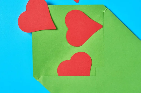 Open green postal envelope and red paper hearts on blue desk. Love message. Concept of Valentines Day. Close-up