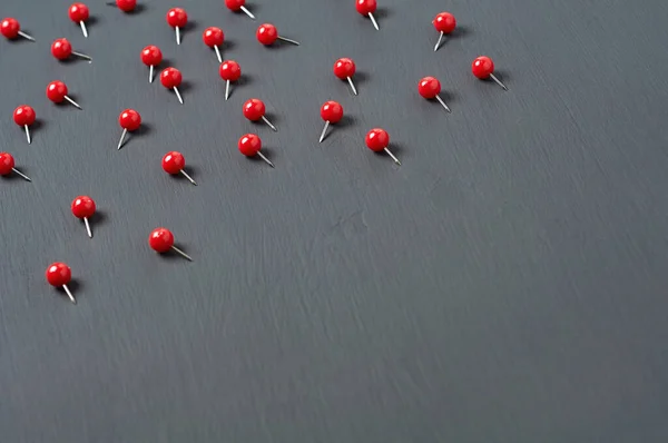 Scattered many red push pins on dark concrete desk in office, school or home. Space for text