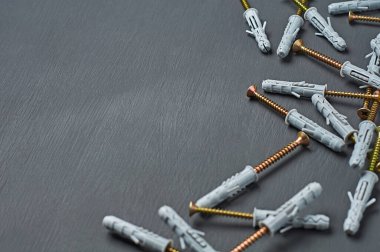 Duvardaki farklı yırtıcıları onarmak için parlak vida rengine sahip bir sürü yeni plastik gri kaplama atölyedeki koyu beton masa üzerinde uzanır. Metin için boşluk