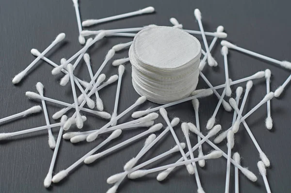 Heap of clean cotton pads and scattered sticks lies on dark concrete desk. Close-up