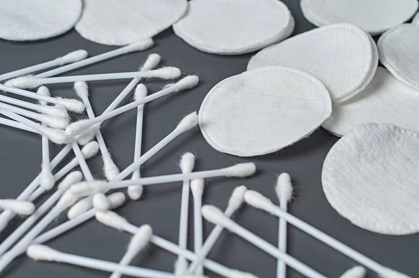 Scattered clean cotton pads and sticks lies on dark concrete desk. Close-up