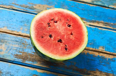 Olgun sulu ve tohumlu karpuzun yarısı aşınmış eski mavi ahşap masanın üzerinde yatıyor. Yakın plan.