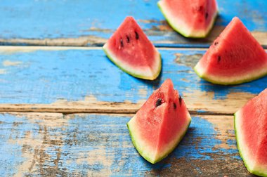 Dağıtılmış olgun sulu karpuz parçaları eski, yıpranmış mavi ahşap masanın üzerinde duruyor. Metin için boşluk