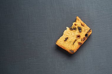 Kırık ev yapımı kuru üzümlü tatlı ekmeğin yarısı mutfaktaki koyu beton masada yatıyor. Mesaj için yer var. Düz yatıyordu