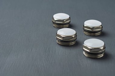 Bimetalik veya alüminyum kalorifer için plastik halkalar ve beyaz plastik kapaklı altıgen metal fındık formundaki dört koçan atölyedeki koyu beton masada yatmaktadır. Metin için boşluk