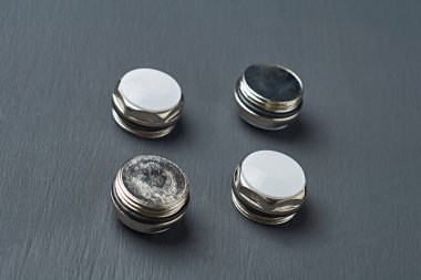 Bimetalik veya alüminyum kalorifer için plastik halkalar ve beyaz plastik kapaklı altıgen metal fındık formundaki koçanlar atölyedeki koyu beton masanın üzerinde yatmaktadır. Yakın plan.