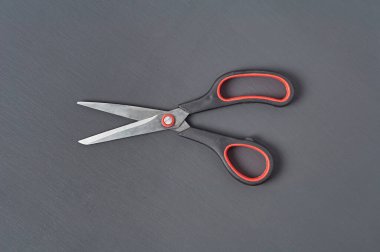 Plastik saplı tek keskin makas siyah ve kırmızı renkler koyu beton masanın üzerinde yatar. Üst Manzara. Yakın plan.