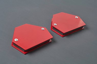 Kaynak yapmak için metal parçaları onarmak için bir çift mıknatıs köşesi atölyedeki koyu beton masada yatıyor. Yakın plan.
