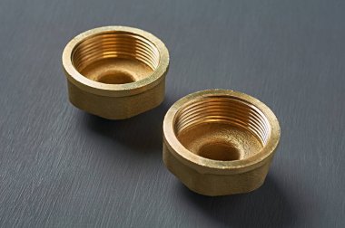 Atölyedeki koyu beton masada küçük ve büyük borular için iplikle tutturulmuş iki bakır ya da bronz boru bulunur. Yakın plan.