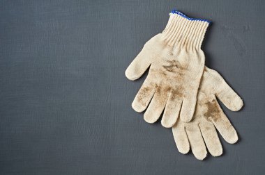 Sıkı çalıştıktan sonra iki kirli beyaz tekstil eldiveni atölyedeki koyu çizik beton masada yatıyor. Mesaj için yer var. Üst görünüm