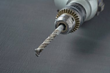 Tamir için eski ve kirli bir elektrikli matkap ya da çengelli delgi veya diğer ağır işler atölyedeki koyu beton masada yatıyor. Yakın plan.