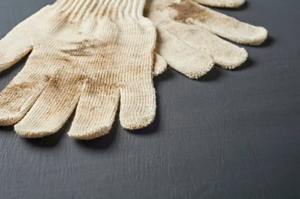Sıkı çalıştıktan sonra bir çift kirli beyaz tekstil eldiveni atölyedeki koyu çizik beton masada yatıyor. Metin için boşluk