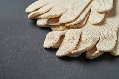 Sıkı çalışma için bir yığın koruyucu beyaz tekstil eldiveni atölyedeki koyu çizik beton masada yatıyor. Metin için boşluk