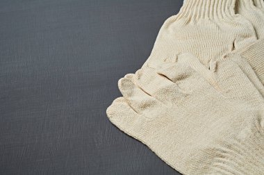 Sıkı çalışma için bir yığın koruyucu beyaz tekstil eldiveni atölyedeki koyu çizik beton masada yatıyor. Metin için boşluk
