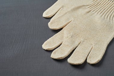 Sıkı çalışma için bir çift koruyucu beyaz tekstil eldiveni atölyedeki koyu çizik beton masada yatıyor. Metin için boşluk