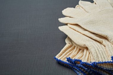 Sıkı çalışma için bir yığın koruyucu beyaz tekstil eldiveni atölyedeki koyu çizik beton masada yatıyor. Metin için boşluk