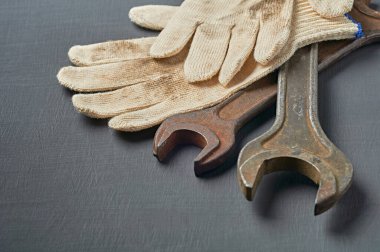 Tamir için bir çift kirli tekstil koruyucu eldiven ya da eski paslı metal anahtarla birlikte çalışma odasındaki koyu çizik beton masada yatıyor. Metin için boşluk