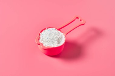 Temizlik bezi için içi çamaşır tozu dolu plastik kepçe, çamaşırhanedeki pembe tezgahın üzerinde yatıyor. Yakın plan.