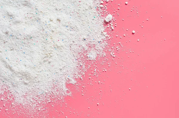 Scattered heap of washing powder for cleaning clothes lies on pink countertop in laundry. Space for text. Top view